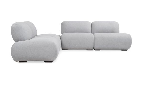 Sala en L Modular Emma con Puff de la marca Aristas vista en perspectiva frontal. Presenta un diseño elegante de líneas curvas, con asientos tapizados en tela suave, patas discretas en madera y un puff que complementa el conjunto.