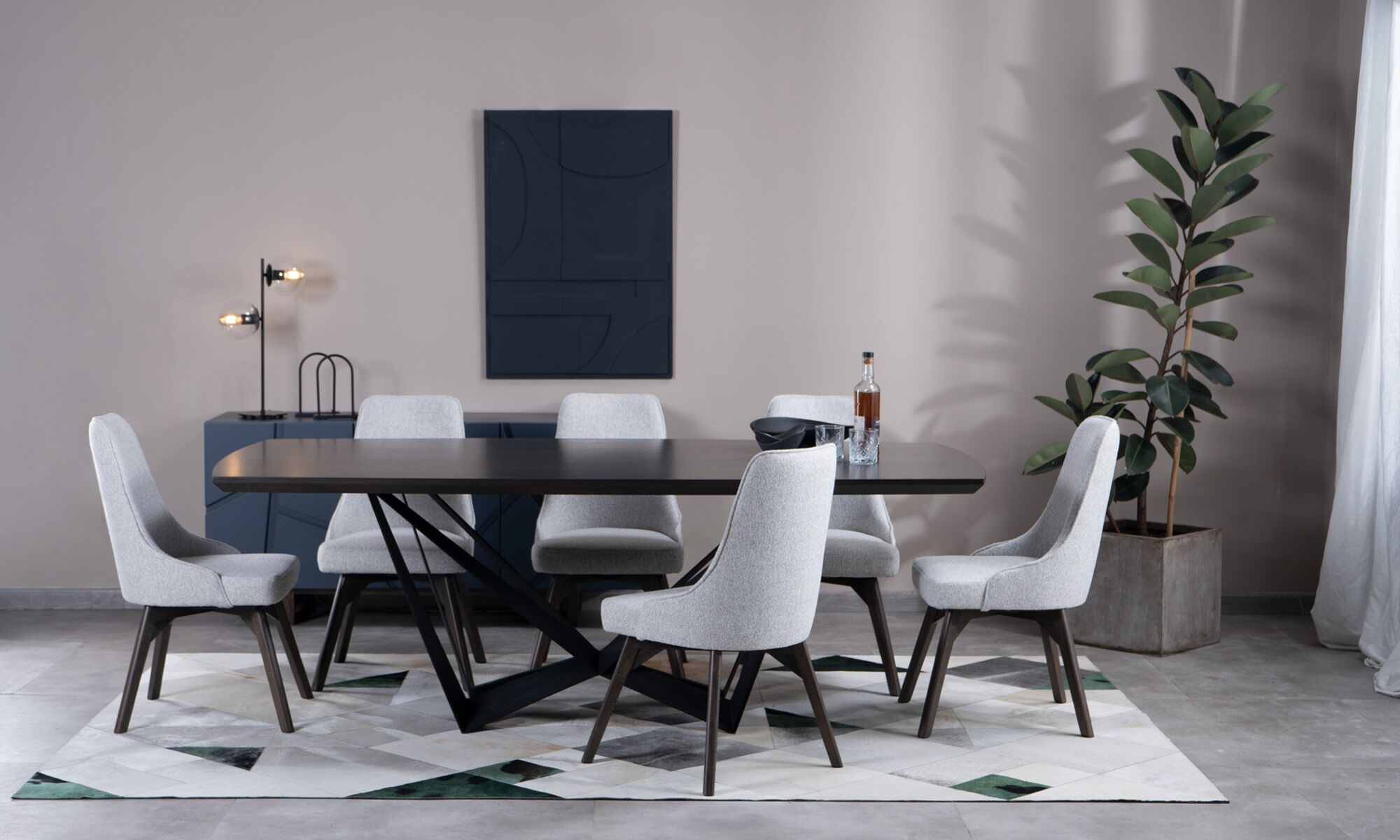 Comedor Versalles + sillas Vela Vista frontal de la Mesa Comedor Versalles con 8 sillas Vela de la marca Aristas. La mesa presenta un diseño rectangular clásico, sostenido por una base moderna y metálica. Las sillas Vela, con respaldo alto y tapizado suave,complementan el conjunto.