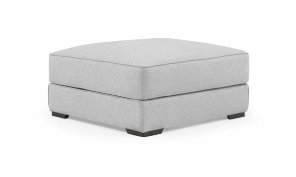 Vista diagonal del Puff Roma de la marca Aristas. Este puff compacto tiene un diseño cuadrado y elegante, con un tapizado uniforme en tono neutro y costuras discretas en sus bordes. Su estructura simple y acolchada ofrece comodidad y versatilidad.