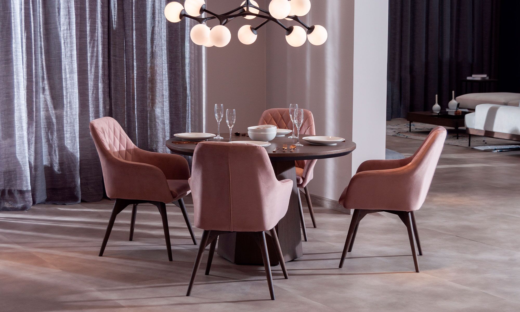 AMBIENTE-COMEDOR-MILANO-REDONDO-4-SILLAS-ODENSE Vista diagonal de la Mesa Comedor Milano Redonda con 4 sillas Odense de la marca Aristas. La mesa presenta una superficie redonda en roble europeo y una base robusta. Las sillas Odense, cuentan con respaldos curvos y líneas elegantes.