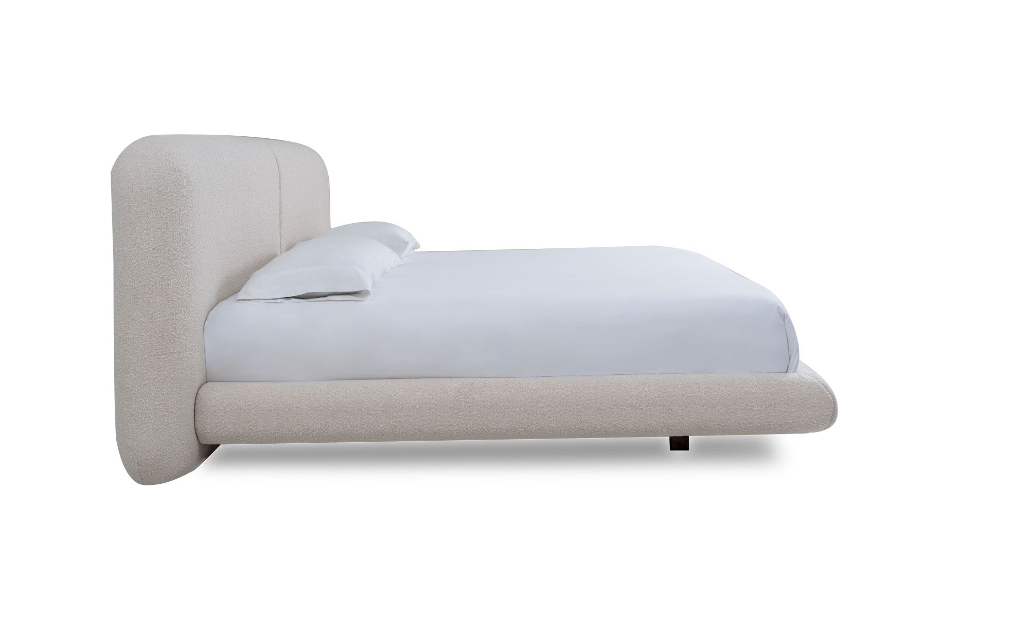 lado MILAN Vista lateral de la Cama Milán de la marca Aristas. Un diseño elegante con una cabecera acolchada de líneas curvas, un tapizado suave y patas discretas en madera.