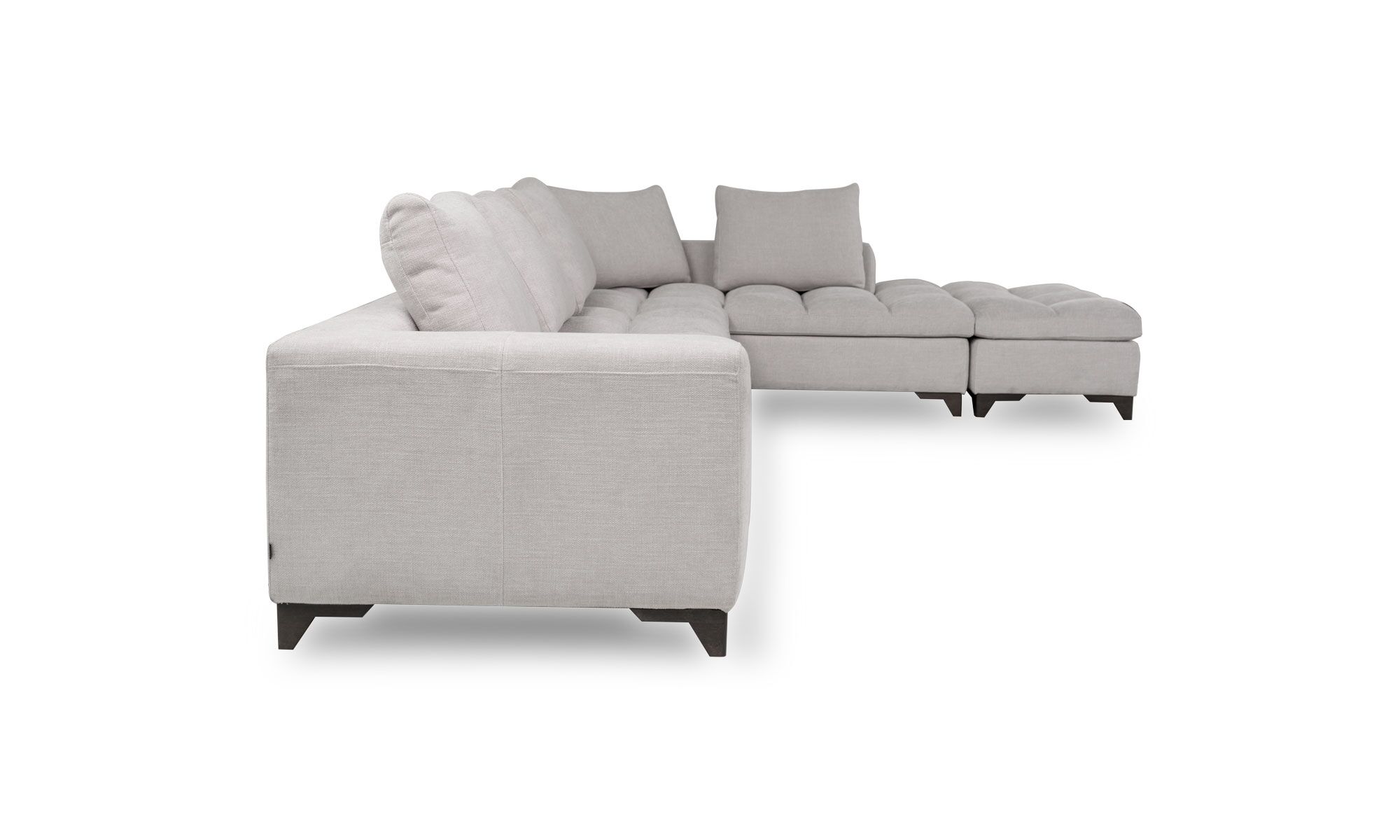 Modular Con Puff Vitaro lado Vista lateral del Modular con Puff Vitaro Plus Plumas de Aristas. Este conjunto modular presenta un sofá amplio, con un puff complementario, ambos en un estilo moderno. El diseño destaca por su tapizado suave y elegante, su asiento acolchado y sus cojines de respaldo.