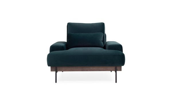 Vista frontal de la Poltrona Maia de la marca Aristas. Presenta un diseño moderno y elegante, con cojines amplios y acolchados. Su estructura se apoya en una base de madera y patas delgadas en metal.