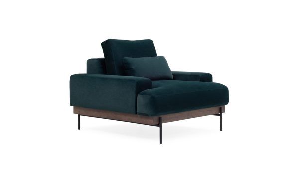Vista diagonal de la Poltrona Maia de la marca Aristas. Presenta un diseño elegante, con cojines amplios y un acabado en tela suave. Está sostenida por patas delgadas que complementan su estilo contemporáneo.